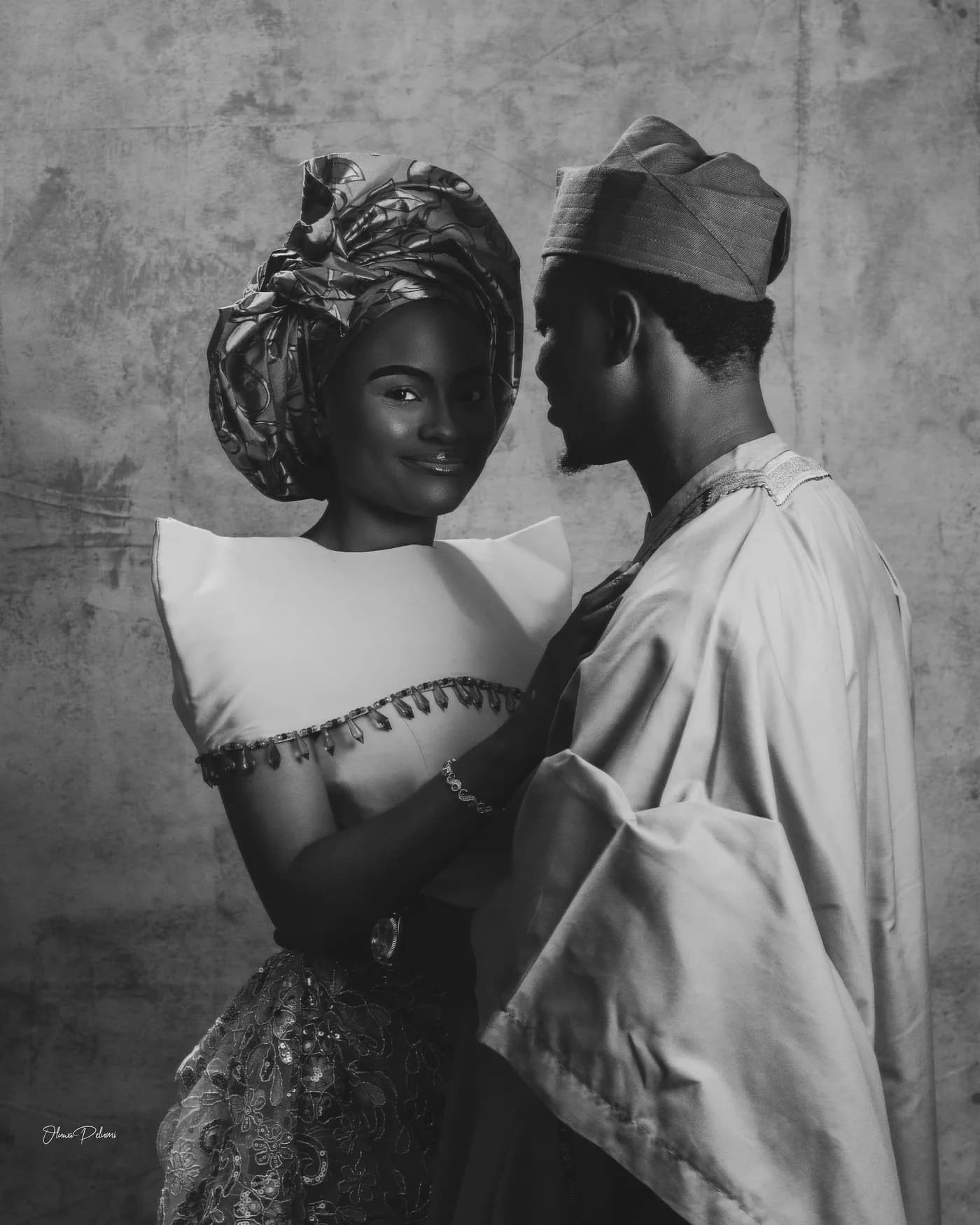 Asepe leaning close to Ajibola, in gele and aso-oke